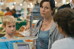 Sascha steht mit seiner Mutter vor der Kassiererin im Supermarkt