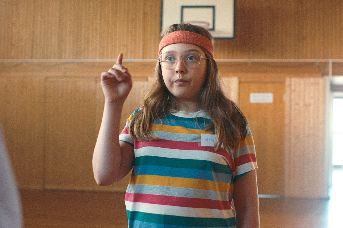 Mina mit Stirn-Schweißband hebt in der Turnhalle den Finger