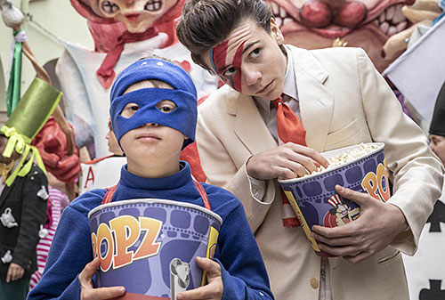 Gio im Superhelden-Kostüm mit einem Bottich Popcorn, dahinter Jack, ebenfalls mit Popcorn